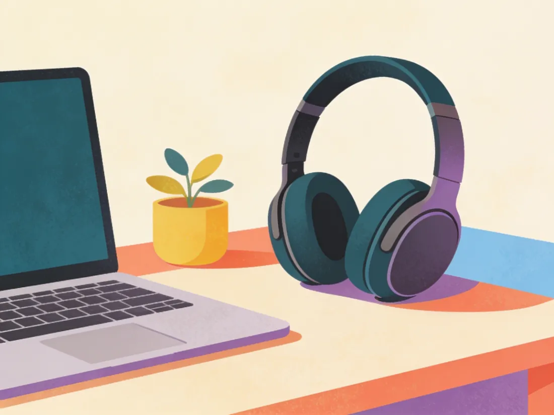 Noise cancelling headphones resting on a desk next to a laptop and a plant.